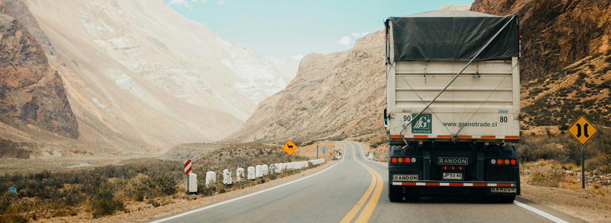 Caminhão em estrada sinuosa de serra, demonstrando as condições de rotas perigosas com curvas fechadas e descidas íngremes em áreas montanhosas