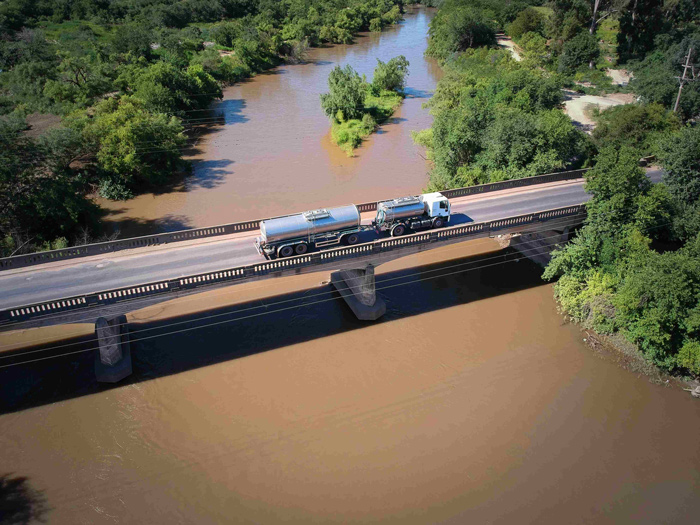 Imagem que retrata otimização de rotas, mostra visão aérea de caminhão em ponte, rota inteligente que reduz quilometragem, consumo de combustível e emissões.