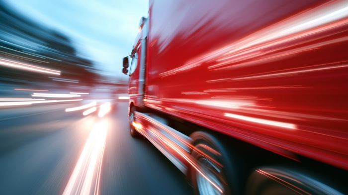 Caminhão vermelho em movimento na estrada ilustrando a importância do controle de velocidade para segurança no transporte rodoviário 