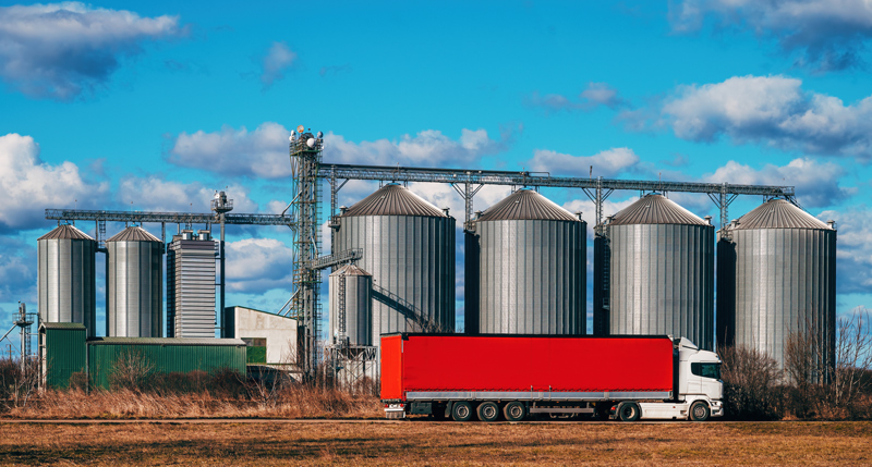 Caminhão de transporte rodoviário do agro estacionado em frente silos.