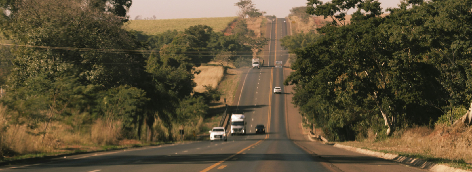 Estrada brasileira com tráfego de carros e caminhões, principal modal de transporte de cargas.