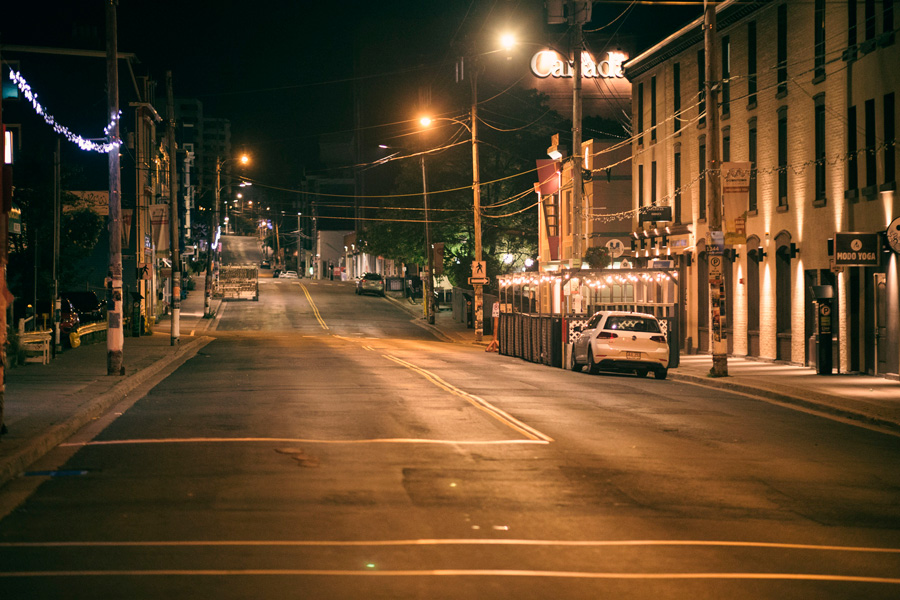 Rua deserta à noite com carro estacionado.