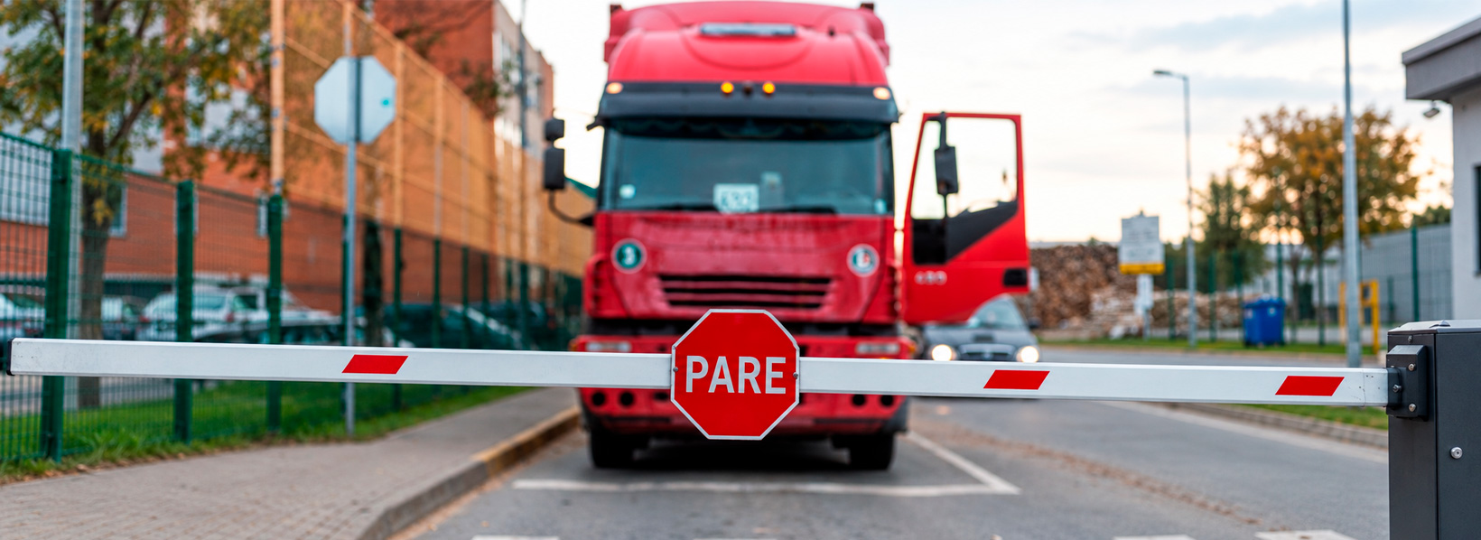 Caminhão vermelho parado em frente bloqueio com placa de PARE, representando a necessidade de parar um veiculo.
